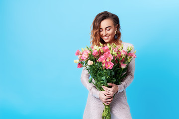 Young happy smiling redhead woman holding bouquet of colorful spring flowers isolated on blue background. Pink roses, festive bouquet in honor of women's day on March 8 or birthday
