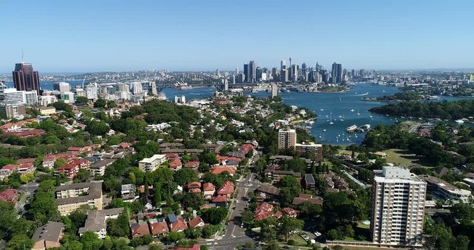 Mid-air landing in residential suburb on Sydney Lower North Shore in view of major city CBD landmarks across Sydney Harbour behind the Bridge.