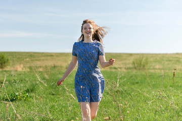 Happy woman with beautiful blonde hair smiling and running on the green meadow
