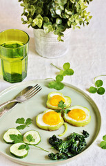 green breakfast on St. Patrick's Day. eggs in the form of clover. Fried Eggs Shamrock  in Green Pepper rings with Braised Spinach. parsley leaves like clover leaves.