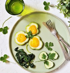 green breakfast on St. Patrick's Day. eggs in the form of clover. Fried Eggs Shamrock  in Green Pepper rings with Braised Spinach. parsley leaves like clover leaves.