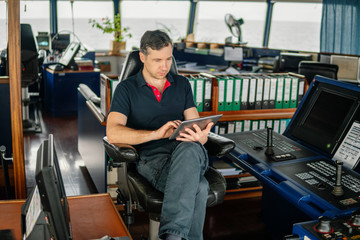 Fototapeta na wymiar Marine chief officer or captain on navigation bridge watching digital tablet. Internet and home connection at sea.