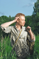 man in an old world war II uniform in a field among tall wild grasses with a big bag in his hands