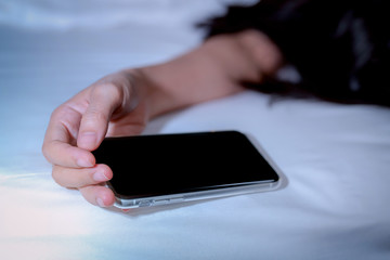 Asian woman sleeping in bed at home and hand holding mobile phone. Woman using smartphone in bedroom. Young woman addicted using smartphone. Texting on cellphone with tired until falling asleep.