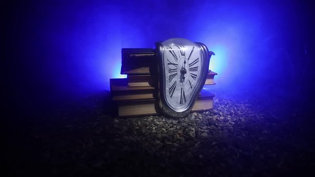 Time Concept. Distorted soft melting clock on a old books, the Persistence of Memory of Salvador Dali. With dark toned foggy background. Selective focus