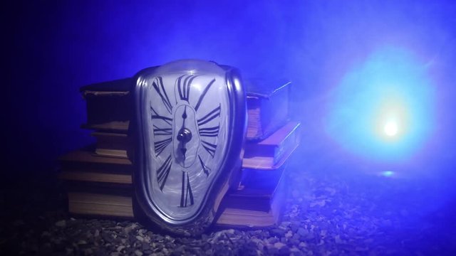 Time Concept. Distorted soft melting clock on a old books, the Persistence of Memory of Salvador Dali. With dark toned foggy background. Selective focus