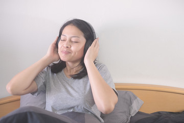 beautiful Asian woman listening music with headphone relaxing on the bed