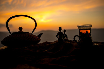 Arabic tea in traditional glass and pot on desert at sunset. Eastern tea concept. Artwork decoration on sand with tea.