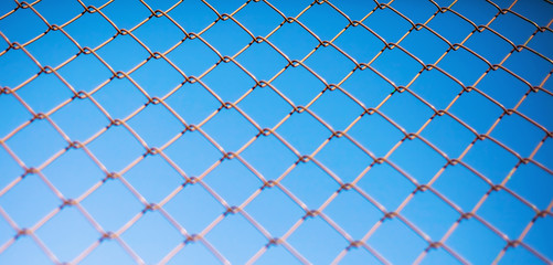 Fototapeta premium The wattled metal gauze of a fencing against the background of the blue sky