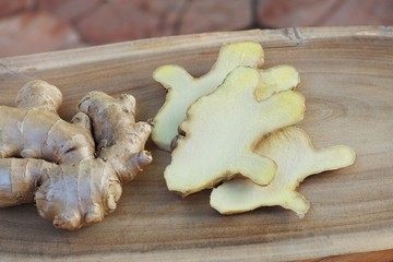 Fresh ginger root and ginger sliced on green leaf background on wood table background, herb concept