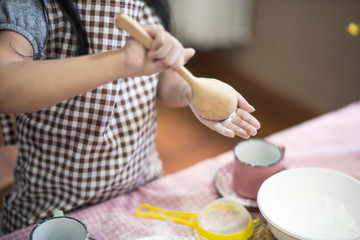 Daughter prepare dough powder by use big spoon take the powder on her hand. She have aprons. Live...