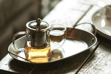 Transparent glass teapot and cup of tea on the stainless steel tray