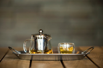 Transparent glass teapot and cup of tea on the stainless steel tray