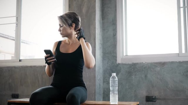Authentic young caucasian woman using her mobile phone in gym to record and chatting to her friend, while resting. Fitness mobile technology concept.
