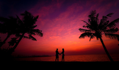 Silhouette of couple on tropical beach during sunset on background of palms and sea