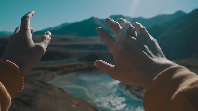 Girl looks at the sun through her hand. View of nature from the first person. A young girl looks at her hands, mountains and river in the background. Slow motion.