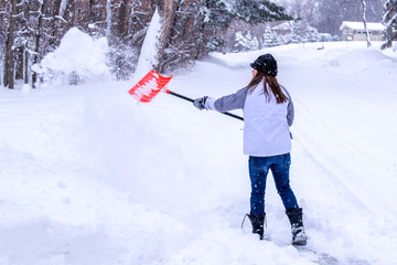 A young gilr is cleaning the snow after a snow storm