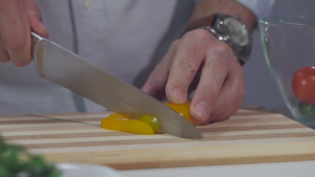A man cuts a yellow pepper with a knife on a divided board.