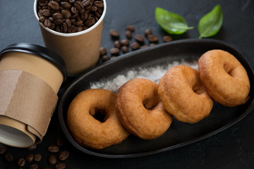 Cast-iron serving pan with donuts and carton takeaway coffee cups, close-up on a black stone surface