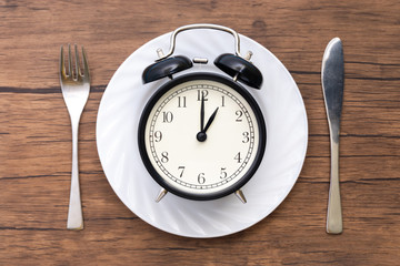 Alarm clock with fork and knife on the table. Time to eat, Breakfast, Lunch time and dinner concept.