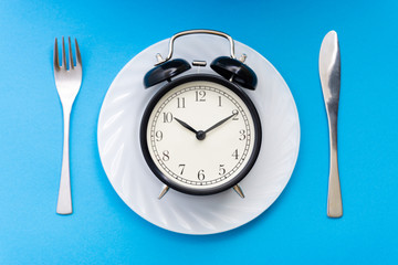 Alarm clock with fork and knife on the table. Time to eat, Breakfast, Lunch time and dinner concept.