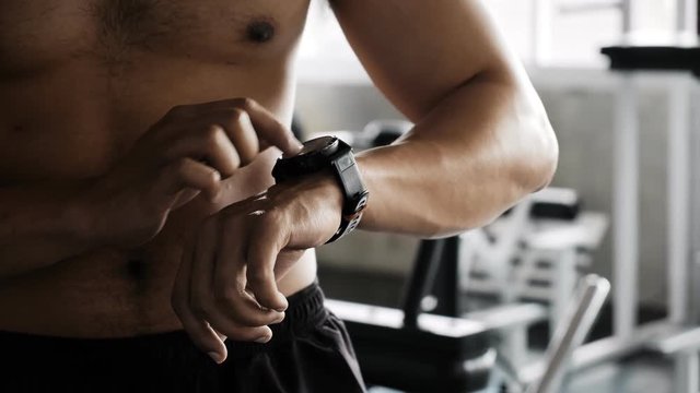 Young asian man using a smart watch in gym. Asian man standing up, touching his watch.