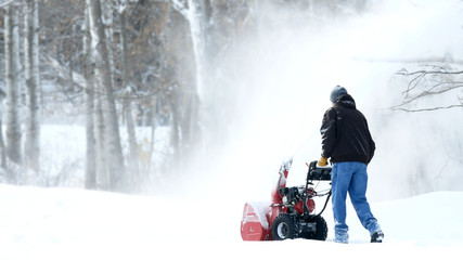 Man works with a snow blower to remove newly fallen snow from driveway after storm in Minnesota.