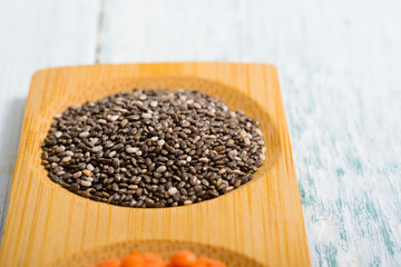 pile of uncooked chia seeds on bamboo, white wooden table
