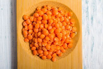 pile of uncooked red lentils on bamboo, white wooden table
