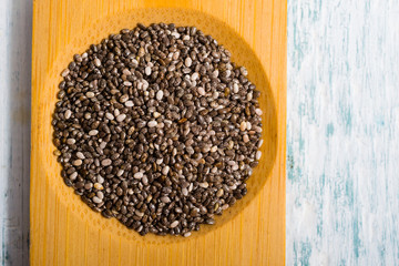 pile of uncooked chia seeds on bamboo, white wooden table