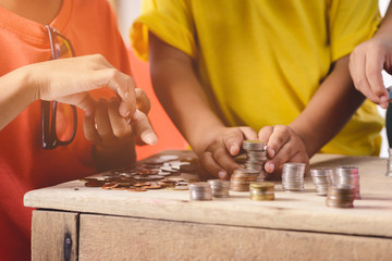 Hands of children are helping putting coins into piggy bank on white background