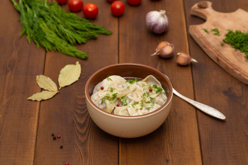 Russian pelmeni meat Dumplings with greens in the plate on wooden table. Tasty homemade meat dumplings.
