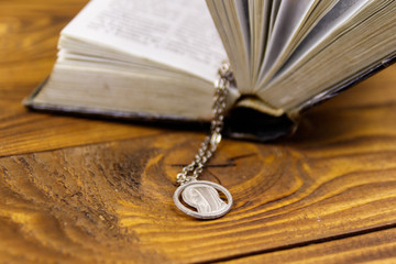 Open Holy Bible with Virgin Mary pendant on wooden background
