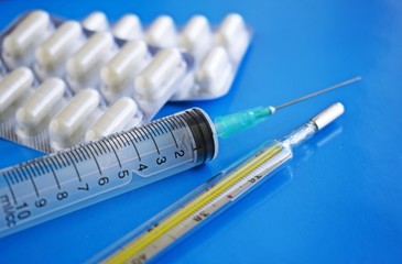 Medical preparation.A syringe and a thermometer on a blue background.