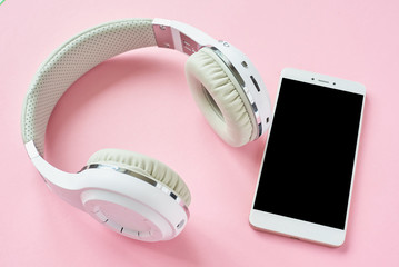 White wireless headphones and smartphone on a pastel pink background