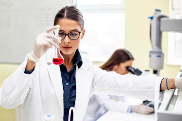 Young woman analyze while second looking at microscope in background