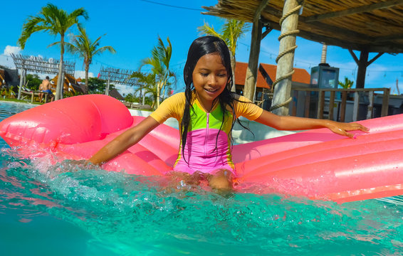 lifestyle outdoors portrait of young happy and cute female child having fun with inflatable airbed in holidays resort swimming pool smiling carefree and cheerful