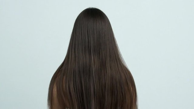 Woman moves long hair. Rear view. Girl shakes long straight hair. Female model is fluttering hair.   Slow motion footage. Rear view.