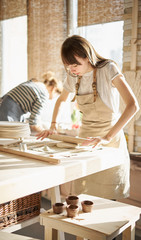 Beautiful young woman making ceramic ware, roll out with a rolling pin in sun light. Concept for woman in freelance, business, hobby