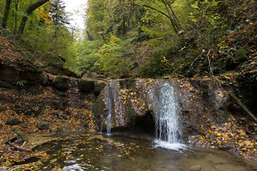 Waterfall on mossy stones in a mountain gorge in the autumn forest.	