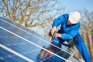 Male engineer in blue suit and protective helmet installing stand-alone solar photovoltaic panel...