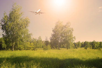 Airliner in the sky over a green field and forest. Sunset in nature.