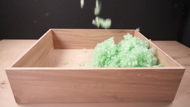 A close-up of green polyester fiberfill falling into wooden box on the black background
