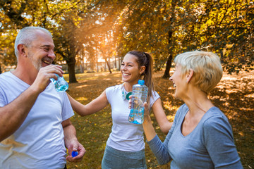 Senior man and woman and young female instructor workout on fresh air, they rest and drink water....