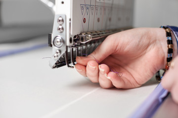 Close-up of female hands filling thread in modern embroidery machine on bright blurred white copy space background. Industrial embroidery, commercial production and high quality results concept.
