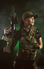 the girl in military special clothes posing with a gun in his hands on a dark background in the haze
