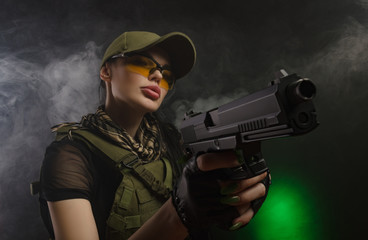 the girl in military special clothes posing with a gun in his hands on a dark background in the haze