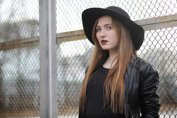A girl walks down the city street in a leather waistcoat with a phone. Young beautiful girl in a hat and with a dark make-up outside. Girl in the Gothic style on street.