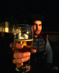 a man holding a glass of beer in a cafe - bar. Focus on beer. Soft colors