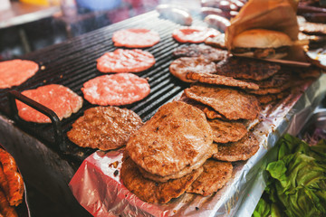 Closeup of traditional street food.Freshly grilled burger and fresh meat ready for grill on barbecue. For sale on gastronomy fair on open street market.